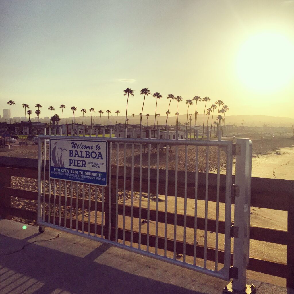 Balboa Pier in the OC with the sun shining early morning and palm trees lined up across the sky.